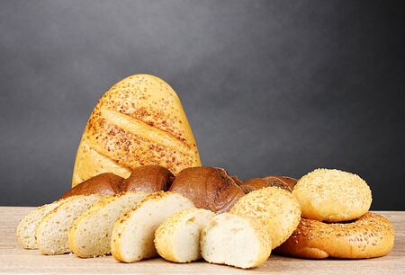 rye and white bread and buns on wooden table on gray background