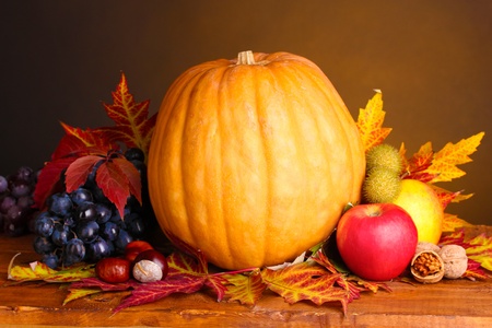 pumpkin, apples, grapes and leaves on wooden table on brown backgroundの写真素材