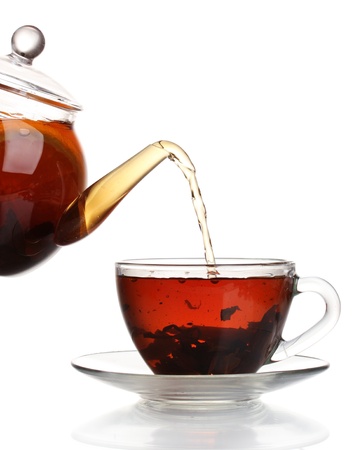 Glass teapot pouring black tea into cup isolated on whiteの写真素材