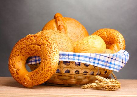 delicious bread in basket and ears on wooden table on gray backgroundの写真素材