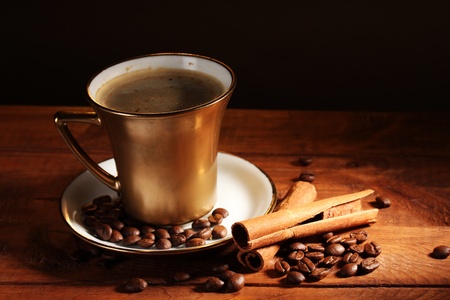 golden cup with coffee, cinnamon and coffee beans on wooden table on brown backgroundの写真素材