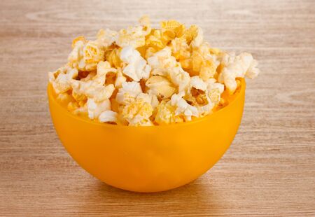 popcorn in bright plastic bowl on wooden tableの写真素材