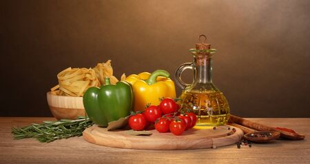 noodles in bowl, jar of oil, spices and vegetables on wooden table on brown backgroundの写真素材