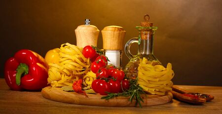 noodles in bowl, jar of oil, spices and vegetables on wooden table on brown backgroundの写真素材