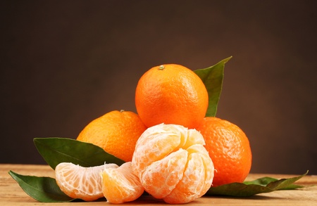tangerines with leaves on wooden table on brown backgroundの写真素材