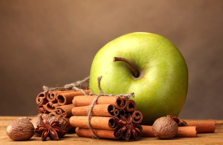 Cinnamon sticks, green apple, nutmeg and anise on wooden table on brown backgroundの写真素材