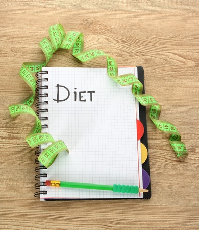 Planning of diet. Notebook measuring tape and pen on wooden tableの写真素材
