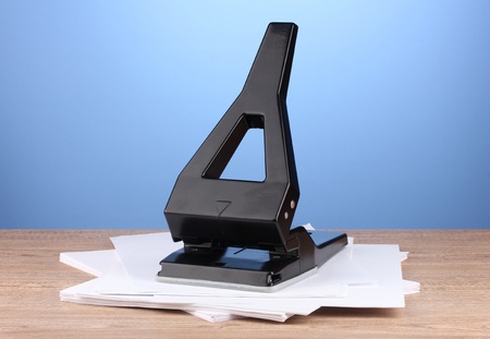 Black office hole punch with paper on blue backgroundの写真素材
