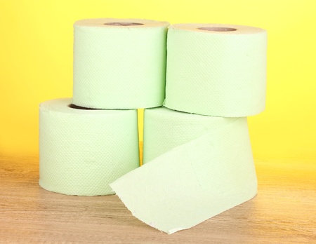 green rolls of toilet paper on wooden table on yellow backgroundの写真素材
