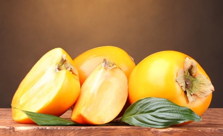 Appetizing persimmons on wooden table on brown backgroundの写真素材