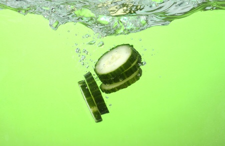 fresh sliced cucumber in water on green backgroundの写真素材