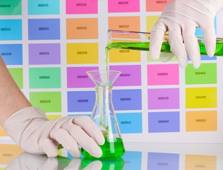 Laboratory flask and tube with green liquid in scientist's hands on color samples backgroundの写真素材