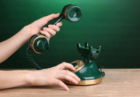 Dialing on retro phone on wooden table on green backgroundの写真素材