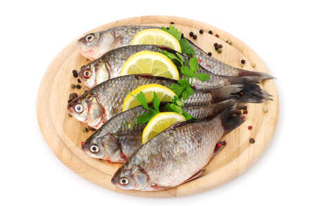 Fresh fishes with lemon, parsley and spice on wooden cutting board isolated on white