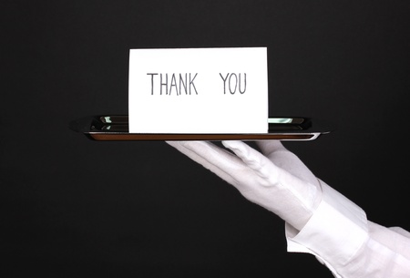 Hand in glove holding silver tray with card saying thank you isolated on blackの写真素材