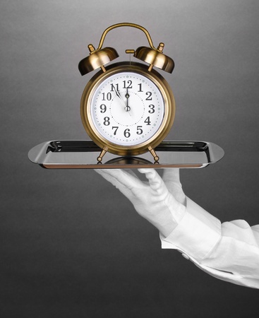 Hand in glove holding silver tray with alarm clock on grey backgroundの写真素材