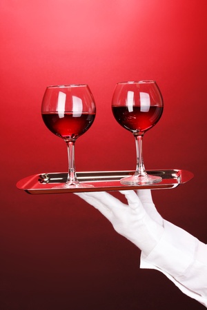 Hand in glove holding silver tray with wineglasses on red backgroundの写真素材