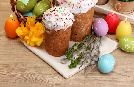 Beautiful Easter cakes, colorful eggs in basket and candles on wooden table