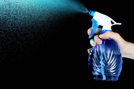 hand holding spray bottle and spraying on black backgroundの写真素材