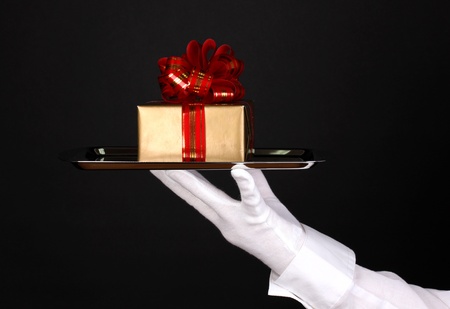Hand in glove holding silver tray with giftbox isolated on blackの写真素材