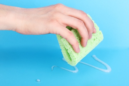 Hand with sponge and poured detergent on blue backgroundの写真素材