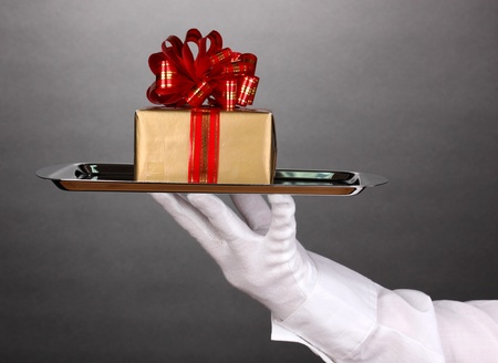 Hand in glove holding silver tray with giftbox on grey backgroundの写真素材