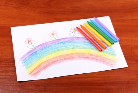 Children's drawing of rainbow and pencils on wooden background