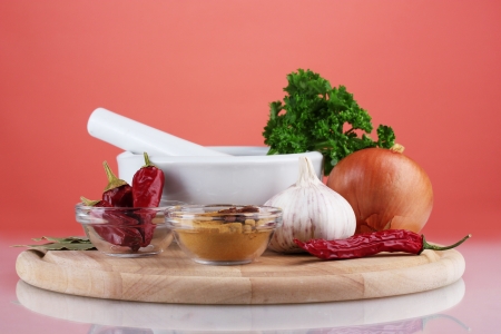 Composition of White mortar and pestle with spice and vegetables on cutting board on red backgroundの写真素材