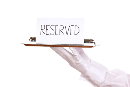 Hand in glove holding silver tray with card saying reserved isolated on whiteの写真素材