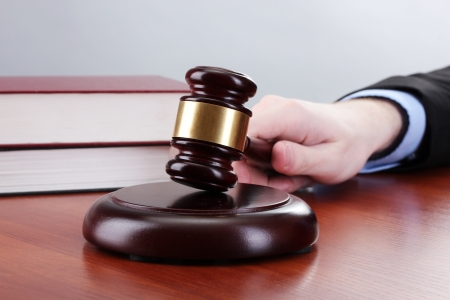 wooden gavel in hand and books on wooden table on gray backgroundの写真素材