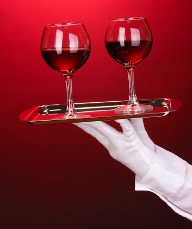 Hand in glove holding silver tray with wineglasses on red backgroundの写真素材