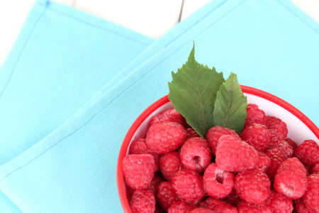 Fresh raspberries in bowl on white wooden background close-up