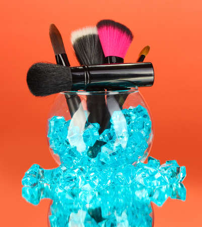 Make-up brushes in a bowl with stones on red background