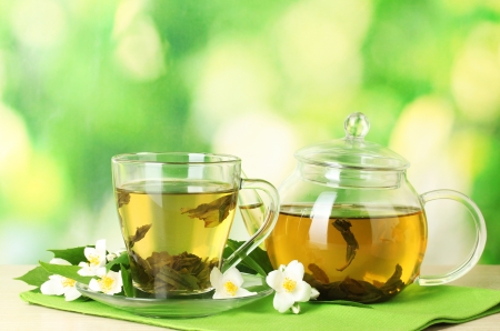 green tea with jasmine in cup and teapot on wooden table on green backgroundの写真素材