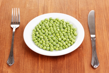 Green peas on plate on wooden backgroundの写真素材