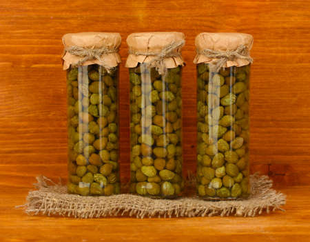 Glass jar with tinned capers on wooden background close-upの写真素材