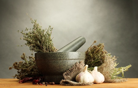 dried herbs in mortar and vegetables, on wooden table on grey backgroundの写真素材