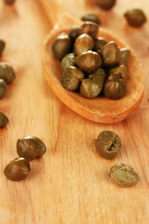 green capers in wooden spoon on wooden background close-up