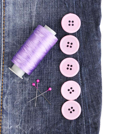 Colorful sewing buttons with thread on jeans isolated on whiteの写真素材