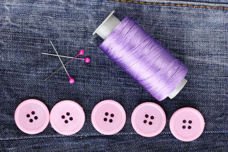 Colorful sewing buttons with thread on jeans closeup
