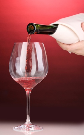 Pouring wine into wineglass on red backgroundの写真素材