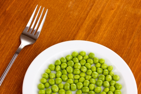 Green peas on plate on wooden backgroundの写真素材