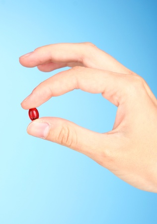 Woman's hand holding a red pill on blue background close-upの写真素材