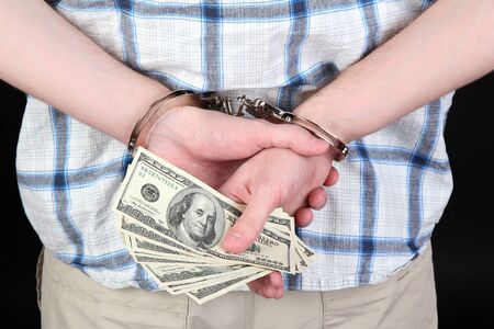 man in handcuffs is holding dollars, on black background