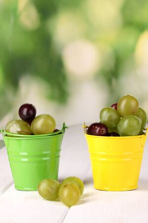 Ripe green and pink grapes in colorful pails on wooden table on natural backgroundの写真素材