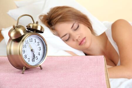 young beautiful woman sleeping on bed with alarm clock in bedroomの写真素材