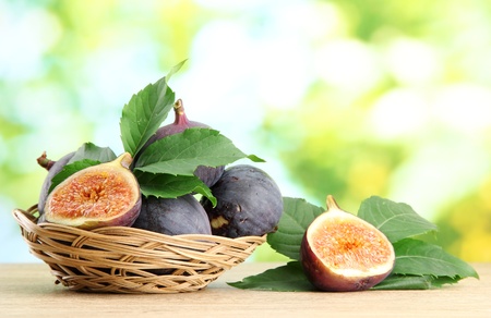 Ripe sweet figs with leaves in basket, on wooden table, on green background