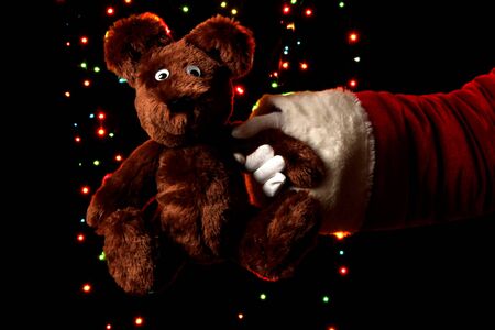 Santa Claus hand holding toy bear on bright backgroundの写真素材