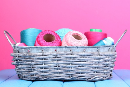 Bright threads in basket on wooden table on pink backgroundの写真素材