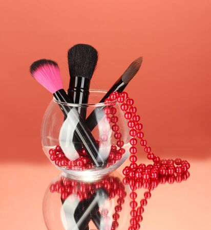 Make-up brushes in a bowl with pearl necklace on red backgroundの写真素材